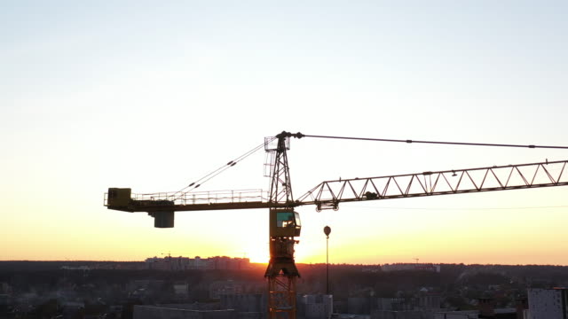 A-construction-crane-swaying-slightly-in-the-wind-against-the-morning-sky.-Close-up,-aerial-video