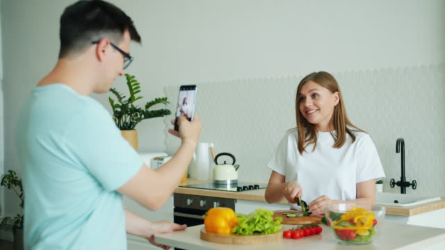Zeitlupe-der-jungen-Frau-kochen-Salat,-während-Mann-fotografieren-mit-smartphone