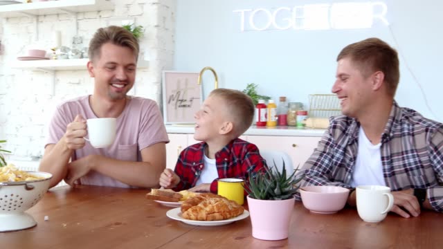 Glückliche-schwule-Familie-zwei-Väter-und-Sohn-frühstücken-in-der-Küche.