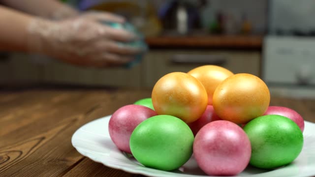 The-girl-paints-chicken-eggs-for-the-Easter-holiday,-in-the-foreground-there-is-a-plate-with-colorful-Easter-eggs,-happiness