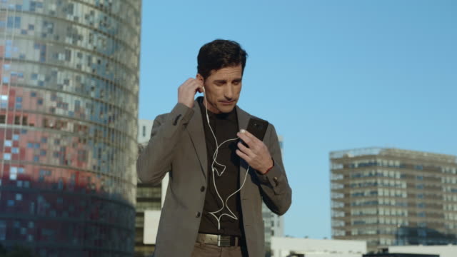 Businessman-walking-with-earphones-on-street.-Employee-using-earbuds-outside