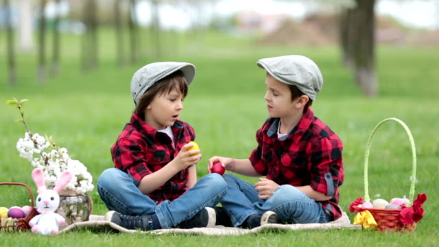 Two-children,-boy-brothers,-having-fun-with-easter-eggs-in-the-park,-beautiful-spring-blooming-garden