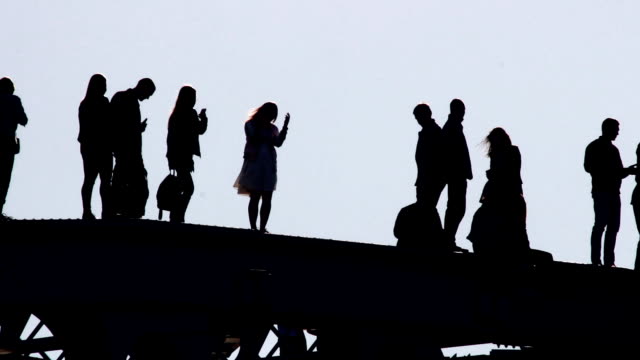 silhouettes-of-young-people-strolling-and-taking-pictures-of-each-other-in-a-precarious-situation-on-the-top-of-the-bridge