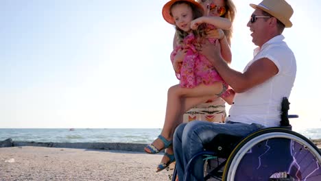 invalid-walk-on-sea-coast,-parents-with-child-on-rest,-happy-pregnant-woman-with-little-girl-and-handicapped-person-in-backlight