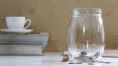 Münzen-in-einem-Glas-auf-dem-Tisch.-Münzen-fallen-in-ein-Gefäß.