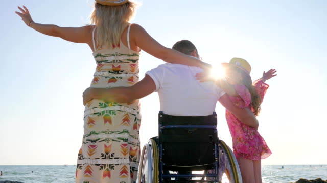husband-in-wheel-chair-hug-wife-and-little-girl-in-backlight,-disabled-hugs-his-wife-and-daughter,-invalid-with-pregnant
