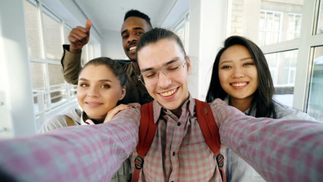 Sicht-der-vier-positive-fröhliche-attraktive-multiethnischen-Freunden-sprechen-Selfie-Fotos-Smartphone-halten-und-Spaß-stehen-im-Flur-der-Universität
