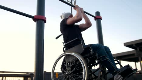 Young-disabled-man-in-wheelchair-engaged-on-the-crossbar-outdoors