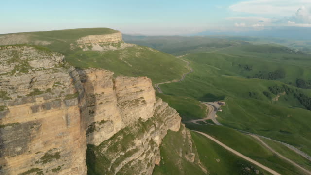 Antenne:-Flug-über-eine-hohe-Felswand,-offenbart-einen-Blick-des-Passes-in-Russland-im-Nordkaukasus.-Luftaufnahmen-von-der-Straße-in-der-untergehenden-Sonne.-Flug-neben-dem-Felsen
