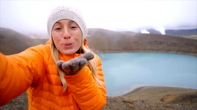 Slow-Motion-junge-Frau-mit-orange-Regenmantel-unter-Selfie-Porträt-mit-Vulkanlandschaft-in-Island.-Die-Leute-reisen-Exploration-Konzept