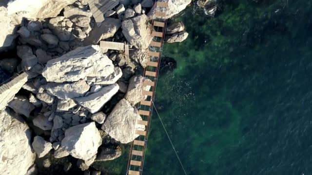 vista-aérea-del-puente-de-cuerda-entre-piedras-y-las-rocas-sobre-las-olas-del-mar-y-el-peligro-de