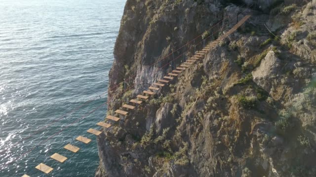 aerial-view-of-rope-bridge-between-the-rocks-over-the-sea-and-danger-waves-and-stones