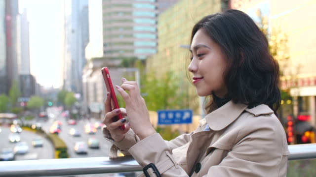 Bastante-feliz-joven-mujer-asiática-mediante-teléfono-móvil-en-la-ciudad-China-de-Chengdu,-en-la-tarde-en-el-puente-con-la-carretera-muy-transitada-en-el-fondo