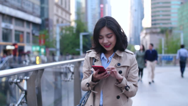 Slow-Motion-ziemlich-glücklich-junge-asiatische-Frau,-die-zu-Fuß-in-der-Stadtstraße-mit-Smartphone-am-Nachmittag