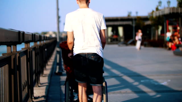 Chico-rollos-de-una-niña-con-discapacidad-con-el-pelo-rojo-en-una-silla-de-ruedas-en-el-paseo-marítimo