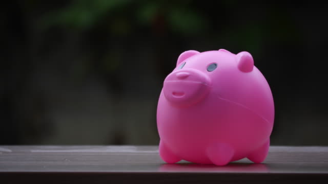 Hand-putting-coins-in-a-pink-piggy-bank,-saving-money-concept
