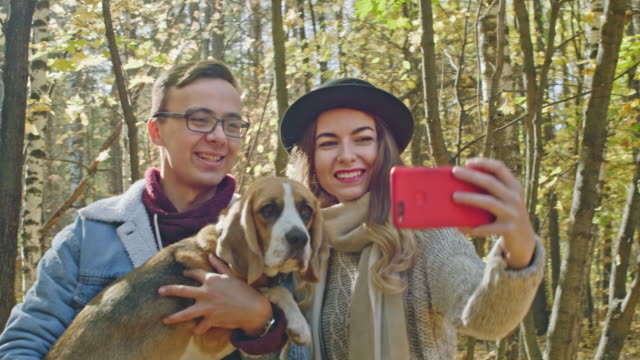 Fröhliches-paar-mit-einem-Hund-nehmen-Foto-im-Herbst-park