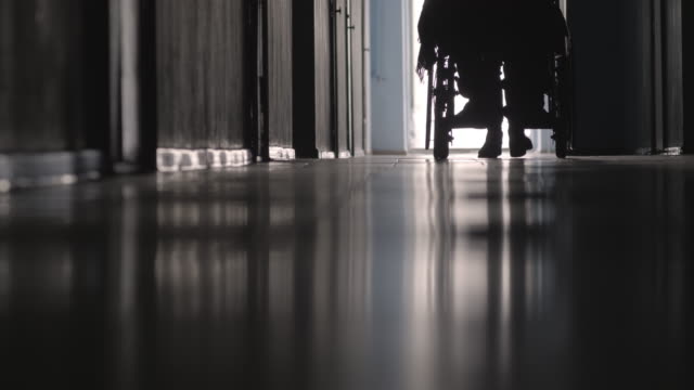 Silhouette-of-Nurse-Pushing-Patient-on-Wheelchair-along-Hallway