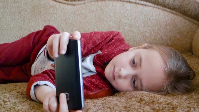 Chica-adolescente-jugando-en-el-teléfono-mientras-yacía-en-el-sofá.