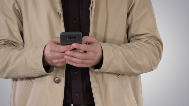 Man-in-trench-coat-using-mobile-smart-phone-on-gradient-background
