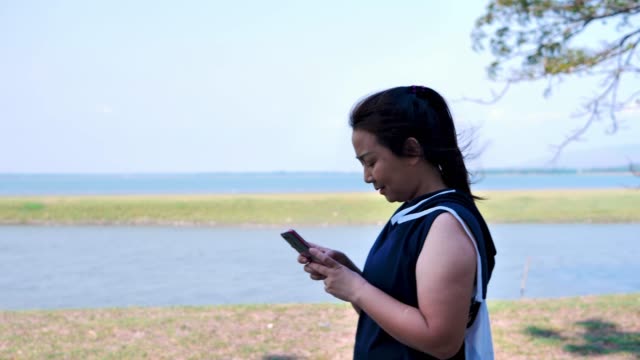 Asiatische-Mädchen-gehen,-trainieren-und-benutzen-das-Telefon-in-der-Natur-mit-der-Sonne-am-Morgen.-Konzept-Gesundheit-mit-Bewegung.-Zeitlupe