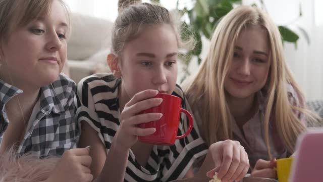 Chicas-adolescentes-bebiendo-café-y-comiendo-palomitas-mientras-ven-contenido-multimedia-en-el-ordenador-portátil