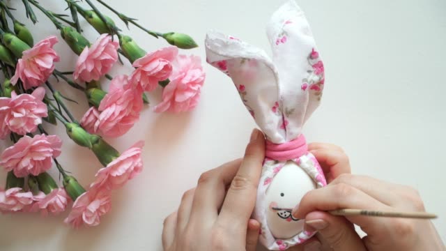Women's-and-children's-hands-hold-chicken-egg-decorated-for-Easter-bunny,-paint-egg-with-brush-pink-cheeks.