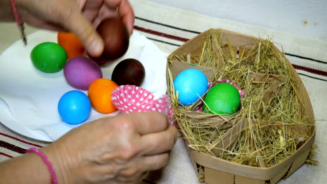 Woman-puts-colorful-Easter-eggs-in-basket-with-hay.