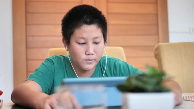 Feliz-niño-Asiático-preadolescente-usando-auriculares-viendo-películas-por-tableta-en-casa.