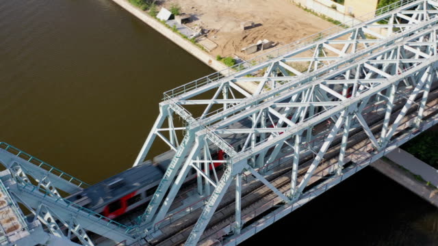 Luftaufnahme-der-Eisenbahnbrücke,-mit-einem-fahrenden-Zug-auf-ihr,-über-den-Fluss,-der-durch-eine-Großstadt-fließt