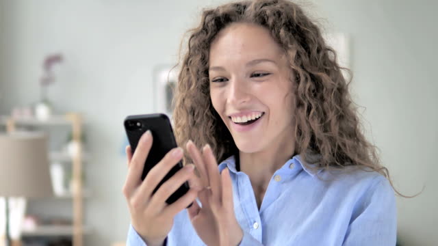 Excited-Curly-Hair-Woman-Enjoying-Success-while-Using-Smartphone