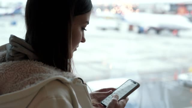 Seitenansicht-brünette-Frau-mit-Smartphone-in-der-Nähe-von-Flughafen-Fenster
