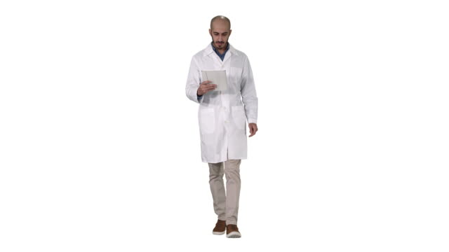 Mature-male-doctor-holding-digital-tablet-using-it-and-walking-on-white-background