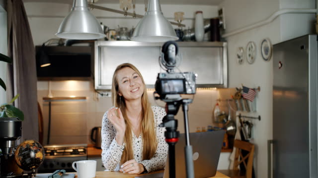 Young-happy-smiling-European-blonde-woman-travel-blogger-talks-recording-new-vlog-for-social-media-at-home-slow-motion.