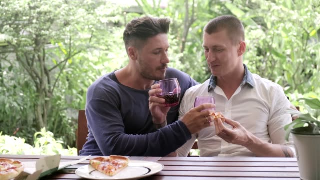 Gay-couple-having-pizza-for-lunch.-Swapping-glasses.