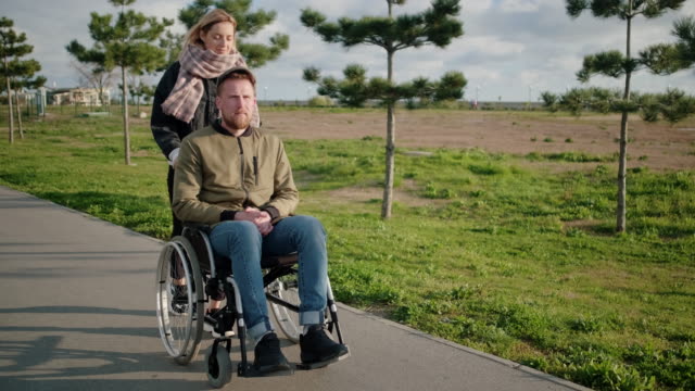 Man-is-sitting-in-invalid-carriage-and-his-wife-is-helping-him,-pushing-it