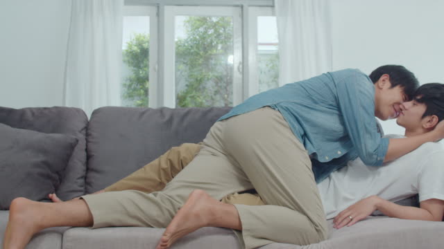 Young-Asian-Gay-couple-hug-and-kiss-at-home.-Attractive-Asian-LGBTQ-pride-men-happy-relax-spend-romantic-time-together-while-lying-sofa-in-living-room-concept.-Slow-motion-Shot.