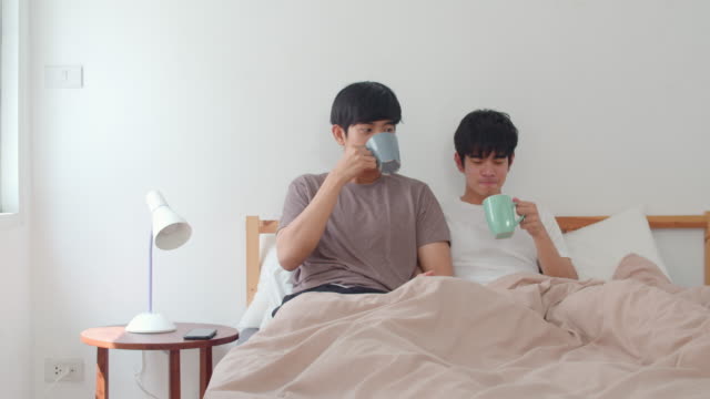 Asiatische-Homosexuell-Männer-Paar-sprechen-mit-einer-tollen-Zeit-im-modernen-Zuhause.-Junge-Asia-Liebhaber-männliche-männliche-entspannen-Ruhe-trinken-Kaffee-nach-dem-Aufwachen,-während-auf-dem-Bett-im-Schlafzimmer-im-Haus-im-Morgen-Konzept-liegen.