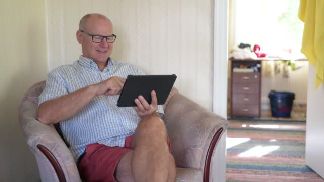 Glücklicher-Senior-Mann-mit-digitaler-Tablet-im-Wohnzimmer