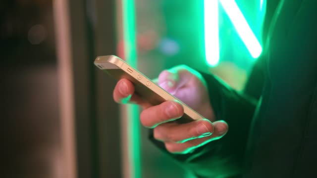 Man-hands-with-smart-phone-close-up-in-trendy-neon-lights-on-street.-Lifestyle.-Easy-pay-online-banking-using-smart-phone-or-digital-device.-Communication-via-app-for-sale-in-shop.-social-media