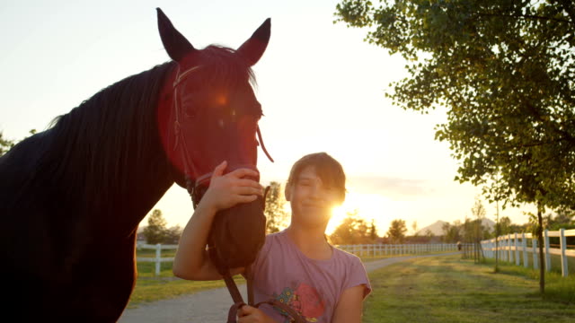 CLOSE-UP:-Fröhliches-kleines-Mädchen-umarmt-schöne-große-braunes-Pferd-bei-Sonnenuntergang