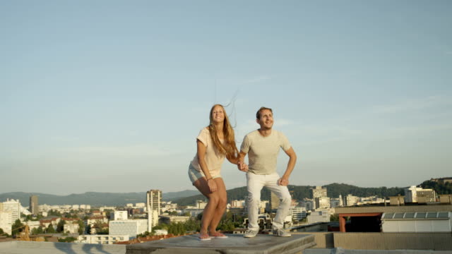 CLOSE-UP:-Two-lovers-holding-hands-and-jumping-on-rooftop-above-the-city