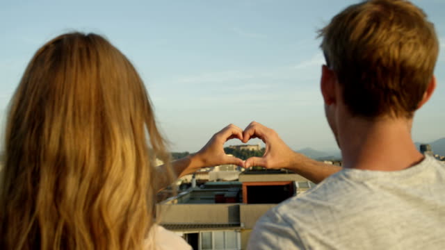 CLOSE-UP:-Young-girlfriend-and-boyfriend-on-rooftop-making-heart-shaped-symbol