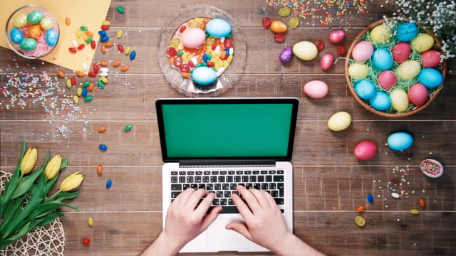 Man-using-laptop-computer-with-green-screen-on-table-decorated-with-easter-eggs-Top-view