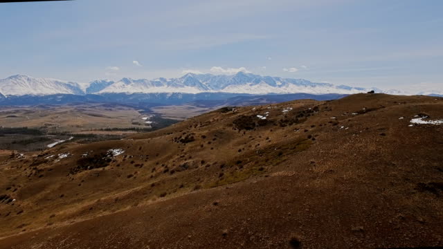 A-flight-over-a-beautiful-valley-with-snowy-mountains-in-the-distance