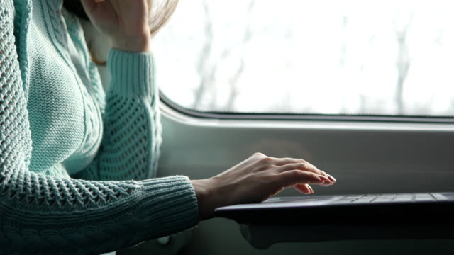 Young-girl-traveling-in-a-train-and-using-notebook.-Female-hands-using-touchpad-of-laptop-pc.-Girl-chatting-with-friends.-Close-up