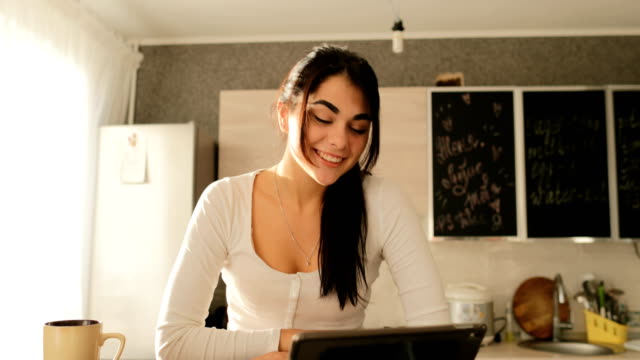 Junge-Frau-machen-Videoanruf-Online-über-Tablet-PC-sitzen-am-Tisch-In-Küche-glücklich-lächelnden-schönen-Mädchen-Morgen-im-Innenbereich