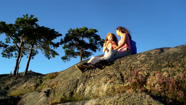 Happy-Female-Couple-Drinking-Champagne-on-a-High-Rock-in-the-Sunshine
