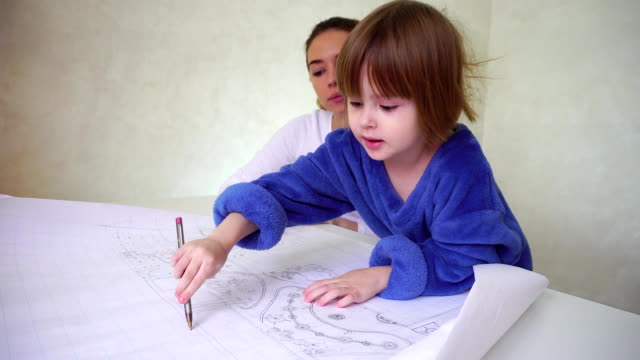Junge-Mutter-hilft-Tochter-mit-Zeichnung,-konzentrierte-sich-Mädchen-sitzt-in-gut-beleuchteten-Raum-diskutieren-Besetzung
