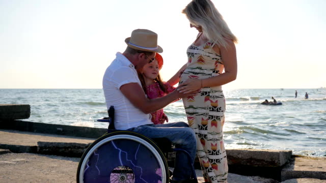 Krüppel-Vater-im-Rollstuhl-und-kleine-Tochter-hört-Bauch-werdende-Mütter,-behinderte-Menschen-und-glückliche-Familie